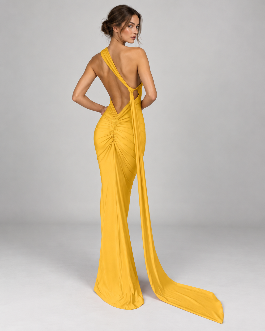Femme portant la Robe Lina jaune vue de dos, avec dos nu plongeant, fronces au niveau des hanches et longue traîne fluide