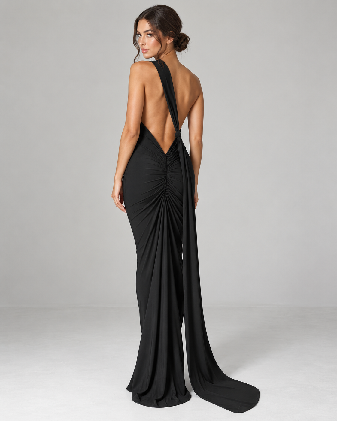 Femme portant la Robe Lina noire vue de dos, avec dos nu profond, fronces centrales et longue traîne pour une allure élégante