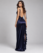 Femme portant la Robe Nina bleu marine satinée, vue de dos, avec dos largement dégagé, fines bretelles à nouer, coupe longue ajustée et volants le long de la fente, pour une silhouette élégante et glamour
