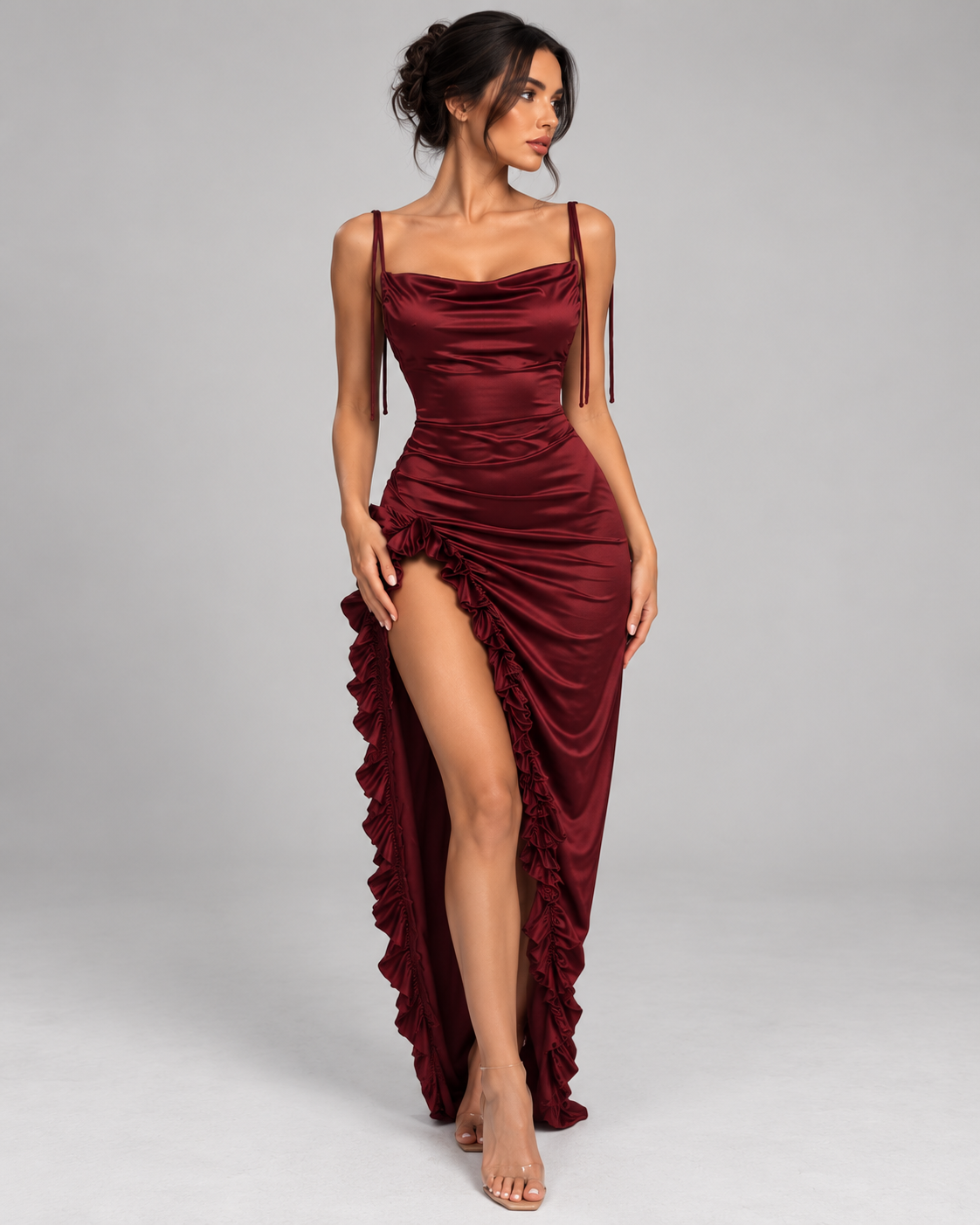 Femme portant la Robe Nina bordeaux satinée, vue de face, avec fines bretelles, encolure drapée, coupe longue ajustée et fente haute bordée de volants, dans un style glamour et sensuel