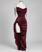 Robe Nina bordeaux satinée présentée sur mannequin, vue de face, avec fines bretelles, encolure drapée, coupe longue ajustée et fente haute bordée de volants