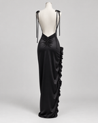 Robe Nina noire satinée présentée sur mannequin, vue de dos, avec dos nu plongeant, fines bretelles à nouer, fronces au bas du dos et volants sur le côté